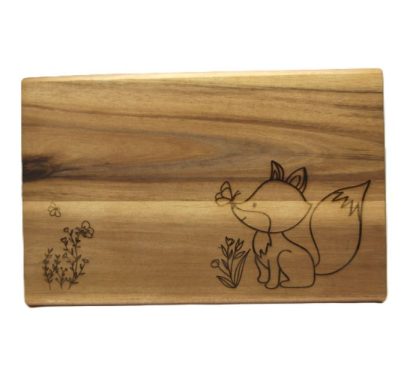 Holzbrett mit eingraviertem Fuchs, der eine Blume betrachtet, umgeben von kleinen Pflanzen.